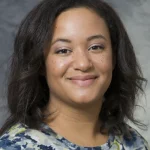 Andrea Gilmore Bykovskyi smiles for her bio picture. She has medium length black hair, and she wears a floral top.