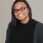 Angel smiles while wearing a black sweater. She has black hair and black glasses.