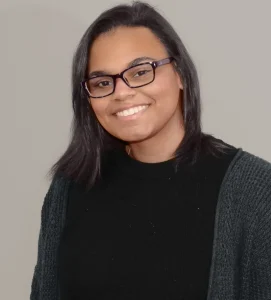 Angel smiles while wearing a black sweater. She has black hair and black glasses.