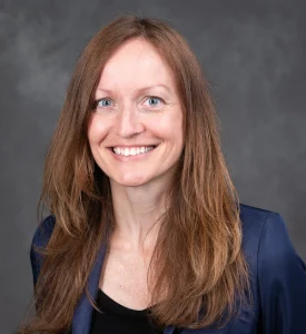 Barb Bendlin smiles for her bio photo. She has long auburn hair and wears a professional blazer.