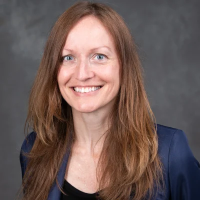 Barb Bendlin smiles for her bio photo. She has long auburn hair and wears a professional blazer.