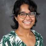 Ruvini Navaratna smiles as she wears a patterned green and white shirt. She has short black hair and black glasses.