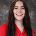 Rachel smiles. She has long dark hair and wears a red blouse.