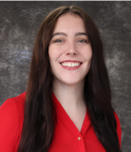 Rachel smiles. She has long dark hair and wears a red blouse.