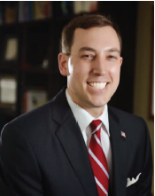 Smiling man in dark suit and red striped tie.