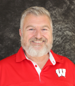 Dave Lyons smiles. He has light grey hair and wears a bright red UW-Madison button up.