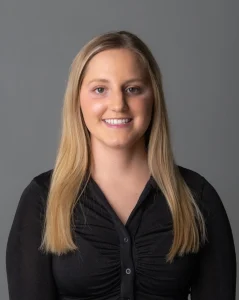 Taylor Moker smiles. She has long blond hair and wears a dark blouse.