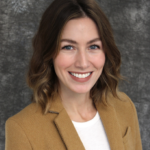 Samantha Mergen smiles widely. Samantha has shoulder length hair and wears a light brown blazer.