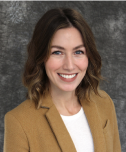 Samantha Mergen smiles widely. Samantha has shoulder length hair and wears a light brown blazer.