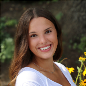 Headshot of a woman with brown hair standing in a wooded garden with yellow flowers